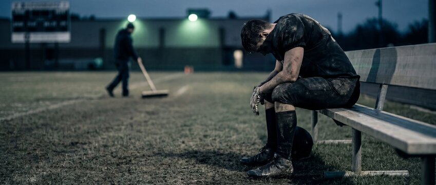 Exhausted american football player sitting on bench after night game. Concept of defeat, burnout, recovery, sports pressure, mental fatigue and athlete resilience. Banner