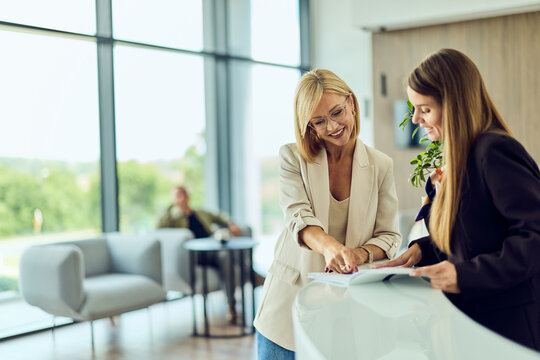 Smiling Client Consulting With Receptionist At Modern Office Lobby Desk For Business Meeting