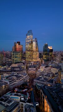 Establishing aerial view of the illuminated City of London, UK, skyline with Bank and Cornhill during twilight dusk
