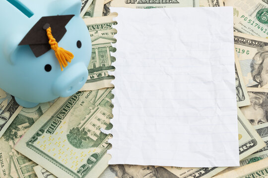 Piggy bank with grad cap with torn blank paper on twenty dollar bills for student loan payments