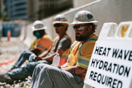 A group of construction workers takes a break in the shade as they hydrate, showcasing the importance of staying cool and alert during extreme heat while on the job.