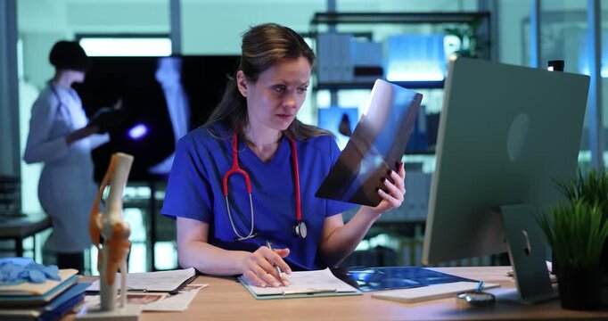 Focused woman doctor looks at x-ray image of patient knee joint in clinic. Female traumatologist analyzes broken bones recovery scan in hospital