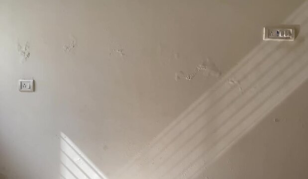Sunlight casting sharp diagonal striped shadows on an indoor dampness moldy patches painted wall