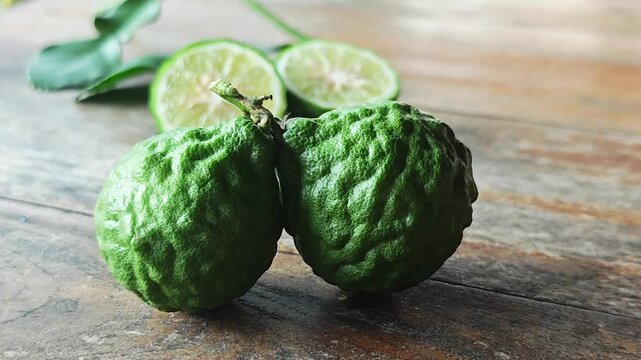 Fresh green kaffir limes with blurred sliced halves on wooden table.