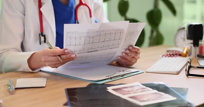 Woman doctor reads patient cardiogram as sits at workplace. Female cardiologist analyzes heartbeat test results at appointment in hospital office