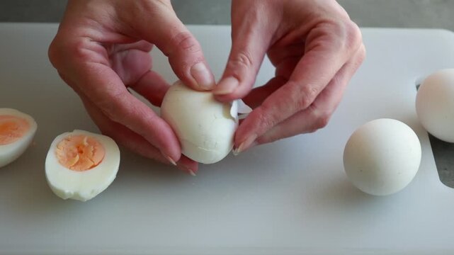 Close-up of a woman's hands carefully peeling the shell off a hard-boiled egg over a clean workspace