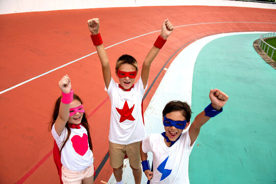 Three excited children in superhero costumes raise fists on a track