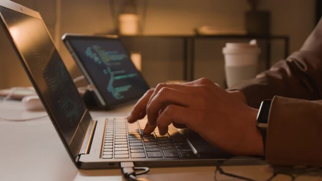 Close-up shot of hands of unknown programmer typing code on laptop keyboard with tablet displaying software scripts in background. Clip for IT startup promotions and cybersecurity marketing