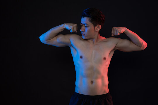 Shirtless athletic man flexing muscles in dramatic blue and red studio lighting