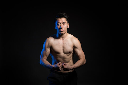 Muscular shirtless man flexing in dark studio portrait