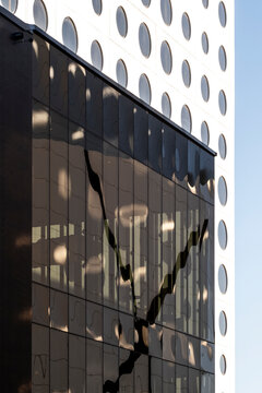 Dark glass facade meets a white dotted building in urban architecture, with windows, reflection, vertical contrast, geometry, and exterior shadow in view
