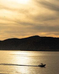 Small motorboat cruising across golden water at sunset with silhouetted hills, Mallorca, Spain © Ricardo