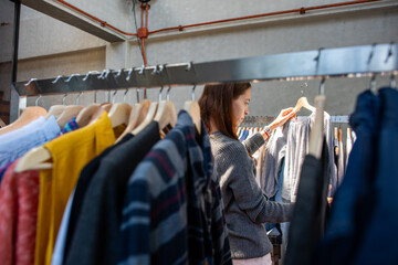 Person browsing clothes on a rack in a store, wearing a gray sweater. © Rawpixel.com