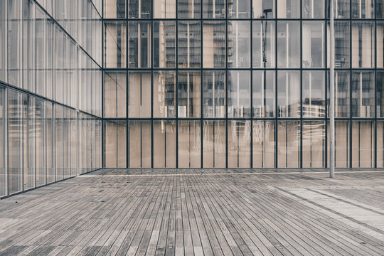 Beyond the wooden deck, a glass facade gives the urban plaza its calm architecture as windows, reflection, grid, and symmetry hold the open space