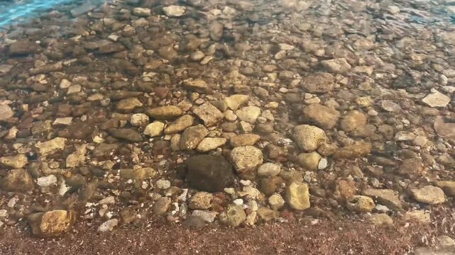 Close-up shot of crystal clear sea water ripples flowing over colorful pebbles on Edirne coast.