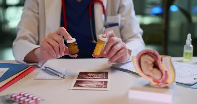 Gynecologist gives vitamin supplements for pregnancy support in clinic office. Woman doctor holds pills bottles near fetus model on table in hospital