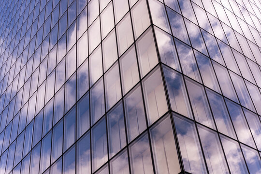 Soft clouds drift through glass reflection on the urban building facade, where windows, grid, sky, and corner lines fold the exterior upward