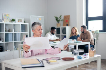 Fototapeta premium Mature businesswoman examining documents in a busy modern office