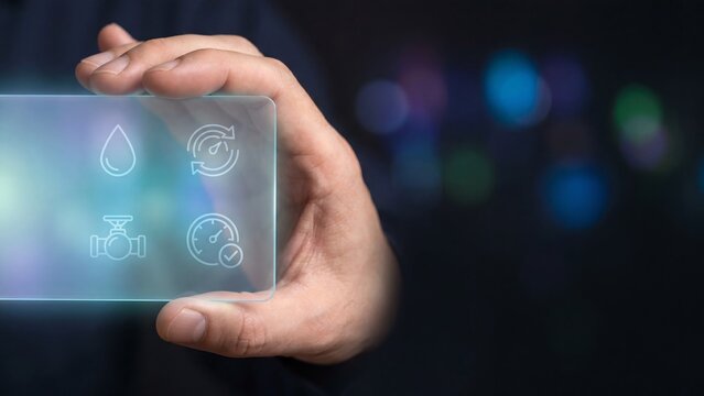 Hand holding glowing holographic water drop, flow meter, valve and gauge icons on transparent virtual panel. Concept of water management, pipeline monitoring, smart utility, and infrastructure control
