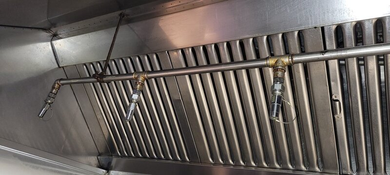 A close-up of the nozzles and piping of a kitchen fire suppression system
