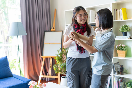 Asian siblings adjusting scarf in bright living room, highlighting family bonding, lifestyle connection, and everyday domestic affection with cozy couch, bookshelves, and natural daylight atmosphere
