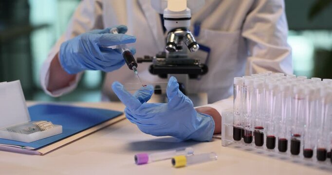Woman medic injects blood onto glass slide with syringe in lab. Female assistant conducts research of patient sample with microscope in laboratory