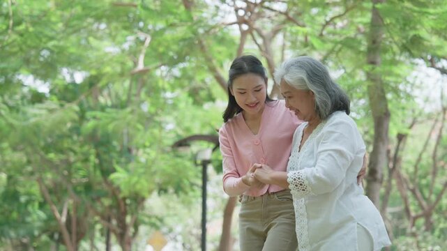 Caring Support: A younger woman gently assists an elderly woman as they navigate a park. A tender moment of support and care, promoting unity and health.