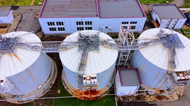 Digester tank tops at wastewater facility. Large corrugated metal cylinder roofs with walkways, piping and access platforms.