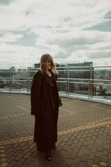 Obraz premium A girl in a black cloak poses on the roof of a building in the city