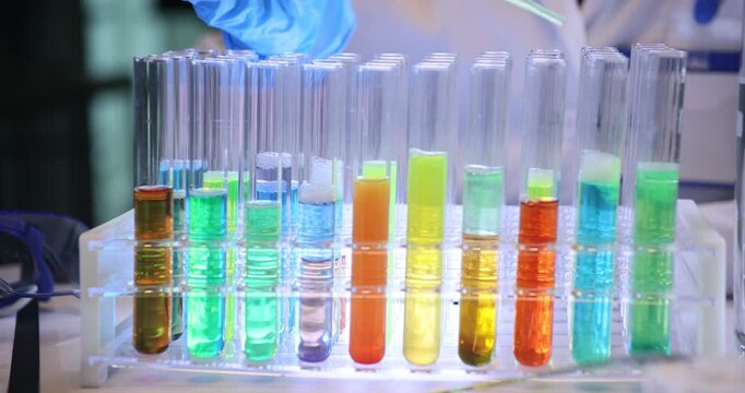 Scientist hand drips reagent into test tubes with color fluids in chemical lab. Assistant conducts research of liquid substances in laboratory