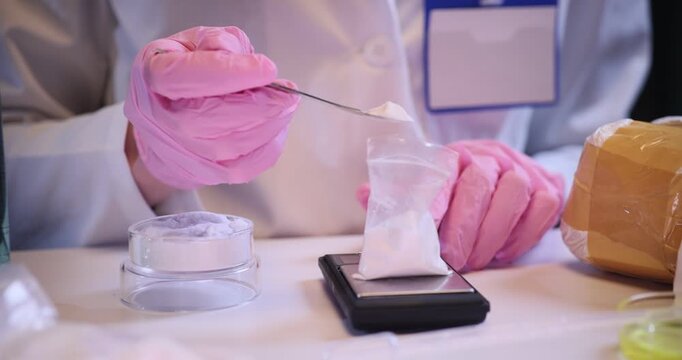 Chemist hands pour white powder into small plastic bag on digital scales in lab. Doctor fills zip package with drugs in criminal laboratory