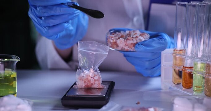 Laboratory worker fills packet with sea salt standing on electronic scales. Lab specialist carefully checks numerical values on scales slow motion