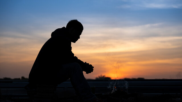 Silhouette of a man sitting by a campfire at sunset, reflecting in peaceful solitude