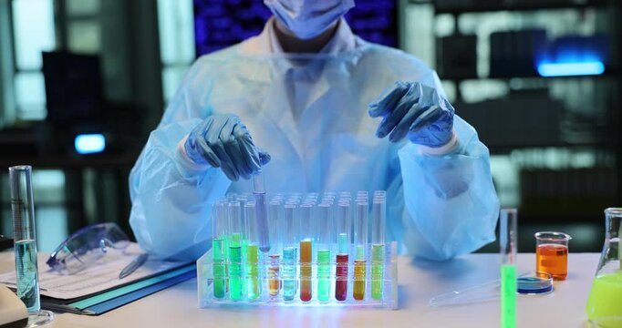 Laboratory worker examines transparent test tubes on rack filled with bright colorful liquids. Experienced specialist observes colorful substances