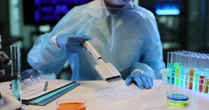 Chemist pours experimental liquid into transparent test tubes. Lab worker uses precise multichannel pipet dispensing device in scientific laboratory