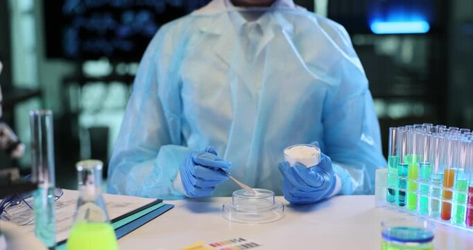 Chemist wearing full protective clothing carefully examines white powder. Scientific specialist studies texture and composition of narcotic powder
