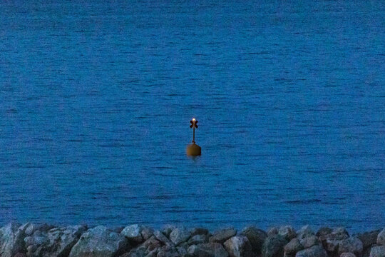 Navigation buoy floating in calm sea beyond rocky breakwater at dusk, Italy, Roseto degli Abruzzi, 28 May 2026