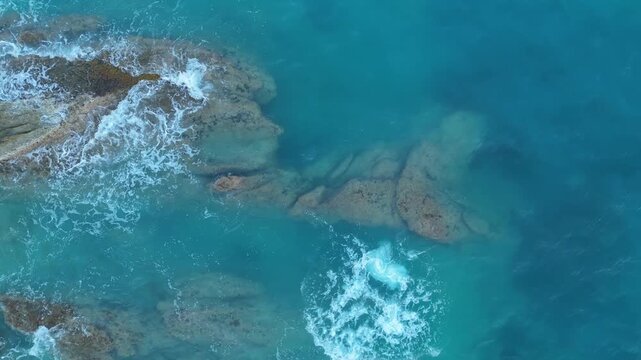 Drone top down view of turquoise ocean waves crashing on rocks