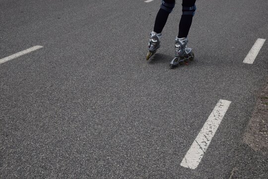 Close-up of person's legs wearing inline roller skates and knee pads skating on an asphalt road with lane markings