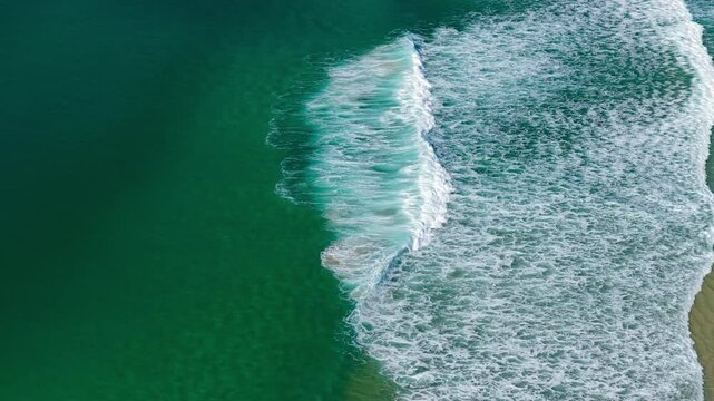 Aerial video capturing the whitewash of rolling waves washing onto the sandy shoreline of One Mile Beach near Forster, NSW, Australia. The movement of the surf creates striking patterns.