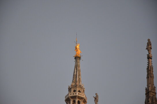 Golden Madonnina statue on the main spire of Milan Cathedral Duomo at sunset.