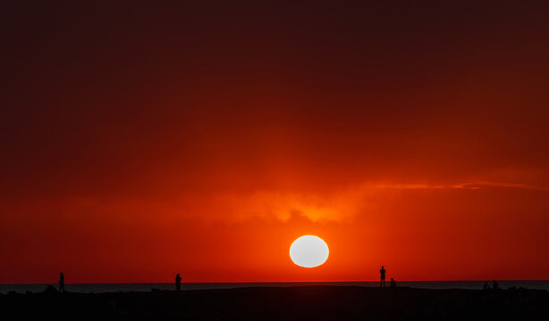 Group of people enjoy sunset on sea beach in Crete. Silhouette of people against setting sun, lifestyle background