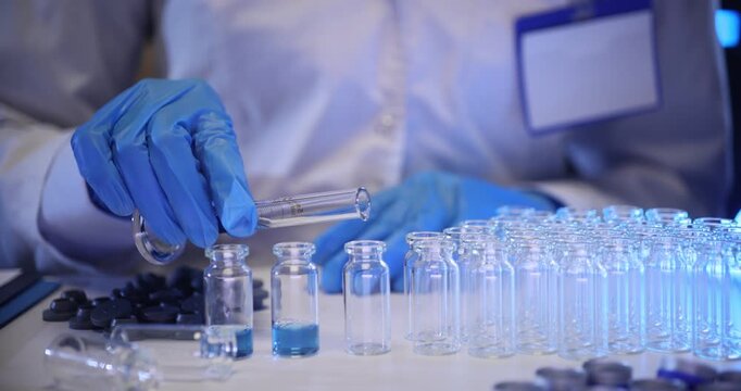 Experienced laboratory employee fills tiny glass vials with blue substance. Professional scientific worker prepares samples for research slow motion