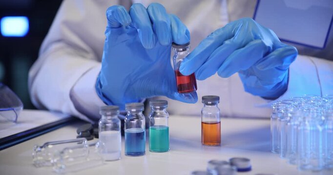 Laboratory worker closes caps on bottles filled with vivid liquids. Lab technician analyzes chemical properties of vibrant multicolored solutions
