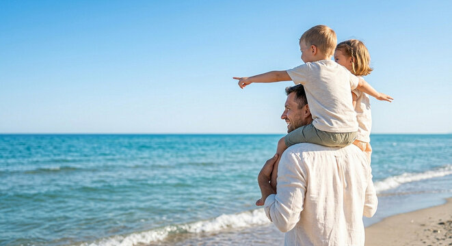 Cheerful father carrying young son on shoulders while standing on sandy beach shore by the blue sea with sister beside, enjoying sunny summer vacation day outdoors
