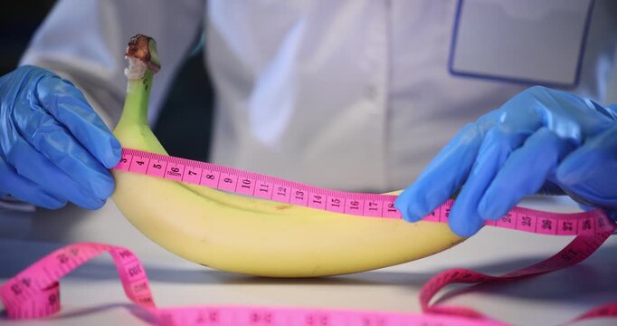 Doctor hands measure banana length with pink tape on table. Physician reminds about healthy eating for wellbeing in hospital office slow motion
