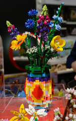 Naklejka premium A bouquet of Lego flowers against a background of multi-colored Lego bricks.
