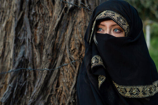 Woman in niqab with blue eyes behind barbed wire
