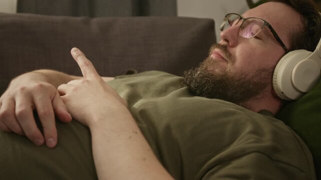 Close up of adult man with diabetes wearing continuous glucose monitor sensor lying down and listening to music in headphones, tilt up camera movement. For diabetes care and health tech marketing
