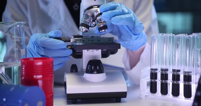Scientist looks at specimen structure in microscope on lab desk. Assistant conducts research of crude oil with magnifying equipment in laboratory